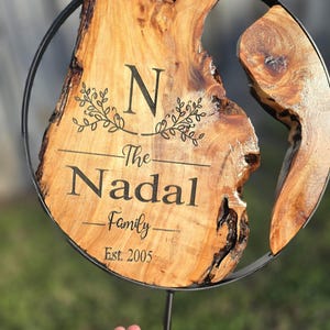 Puede incluir: Un letrero redondo de madera con un anillo de metal alrededor del borde. El letrero está grabado con la letra "N", las palabras "The Nadal Family" y el año "Est. 2005".