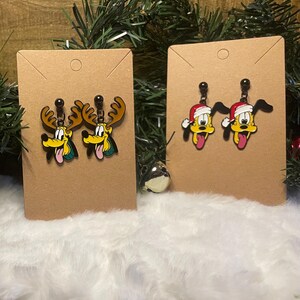 May include: Two pairs of Christmas-themed earrings. One pair features a yellow cartoon dog with reindeer antlers, and the other pair features a yellow cartoon dog wearing a Santa hat. Both pairs are on brown earring display cards.