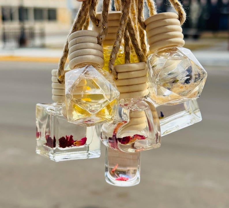 May include: A set of six glass car air fresheners with different shapes and floral accents. The fresheners are suspended from wooden beads and twine.