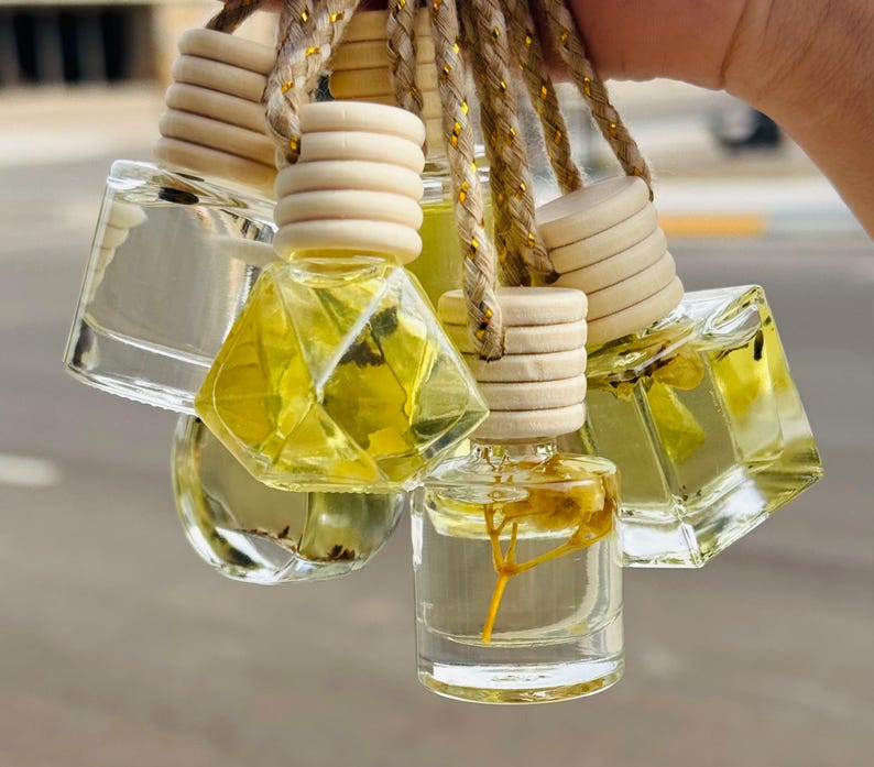 May include: A set of six small glass bottles with wooden tops and a string for hanging. The bottles are filled with a clear liquid and contain dried flowers.