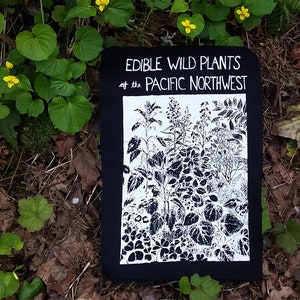 May include: A black and white illustration of edible wild plants of the Pacific Northwest on a black background. The illustration is printed on a black fabric square.