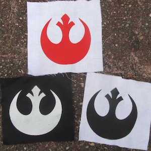 May include: Three fabric patches with the Rebel Alliance symbol from Star Wars. The first patch is white with a red symbol. The second patch is black with a white symbol. The third patch is white with a black symbol.