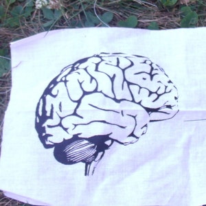 Op de afbeelding: Een witte stoffen patch met een zwart-witte illustratie van een menselijk brein.