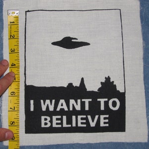 May include: Black and white fabric patch with a UFO silhouette, a black landscape, and the text "I WANT TO BELIEVE".
