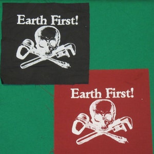 May include: Two fabric patches with the words "Earth First!" and a skull and crossbones design. The skull is white and the crossbones are two white wrenches. One patch is black and the other is red.