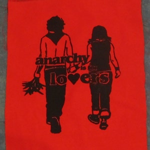 Könnte beinhalten: Ein roter Patch mit einer schwarzen Silhouette von zwei Personen, die gehen. Der Text "anarchy is for lovers" ist in Schwarz mit einem Herzsymbol gedruckt.