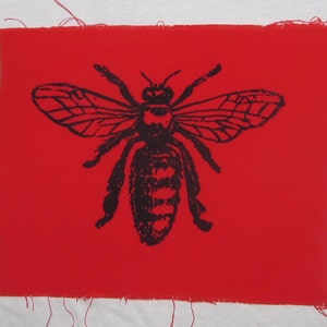 Könnte beinhalten: Ein roter Stoff-Patch mit einer schwarzen Biene als Silhouette.