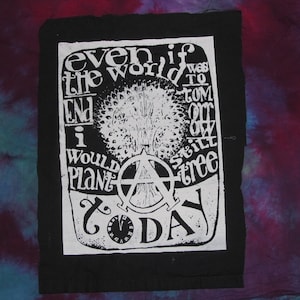 Può includere: Toppa bianca e nera con il testo "anche se il mondo finisse domani, pianterei comunque un albero oggi". Il testo è circondato da un albero stilizzato e un simbolo anarchico.