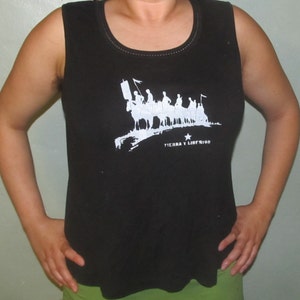 Könnte beinhalten: Schwarzes ärmelloses Tanktop mit einem weißen Aufdruck einer Gruppe von Menschen, die auf Pferden reiten. Der Aufdruck enthält den Text "Tierra y Libertad" und einen Stern.