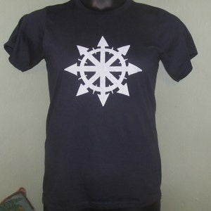 May include: A dark navy blue t-shirt featuring a white, stylized eight-pointed starburst design. The graphic is centered on the chest. The shirt has short sleeves and a crew neck.