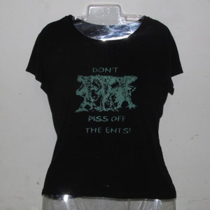 Op de afbeelding: Zwart T-shirt met de tekst "DON'T PISS OFF THE ENTS!" in turquoise. De afbeelding heeft een gestileerd, abstract ontwerp. Het shirt wordt gepresenteerd op een doorzichtige plastic hanger.