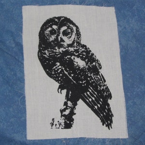 May include: Black and white silhouette of an owl with detailed feathers on a white fabric background.