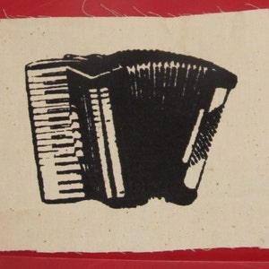 Op de afbeelding: Een zwart-witte accordeon gedrukt op een beige stoffen patch.