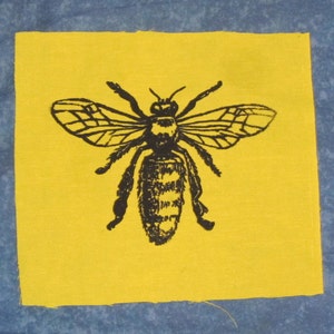 May include: A black and white illustration of a bee on a yellow fabric patch.