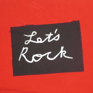 Puede incluir: Parche de tela negro con letras blancas que dicen "Let's Rock".