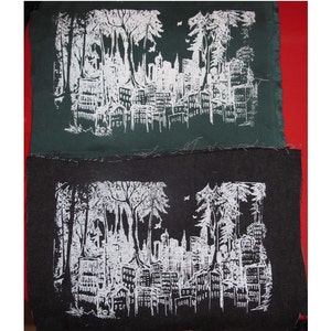 May include: Two black fabric patches with a white design of a city skyline with trees in the foreground. The design is printed on the fabric.