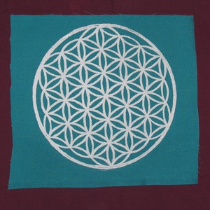 May include: A teal fabric square with a white geometric pattern in the center. The pattern is a flower of life design.