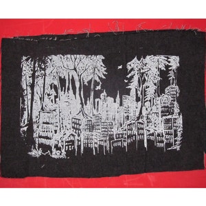 Könnte beinhalten: Schwarz-weiß gestickter Patch, der eine Stadtlandschaft mit Bäumen im Vordergrund zeigt. Die Skyline der Stadt ist in Weiß vor einem schwarzen Hintergrund umrandet.
