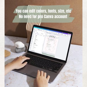 May include: A laptop displaying a menu template with the text "MENU" and "You can edit colors, fonts, size, etc. No need for pro Canva account." The screen shows a menu design with pink accents. Hands are typing on the laptop keyboard.