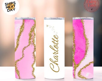May include: Three stainless steel tumblers. Two tumblers feature a pink watercolor design with gold glitter accents. The third tumbler is white with the name "Charlotte" in gold script. The tumblers are cylindrical and have a shiny finish.