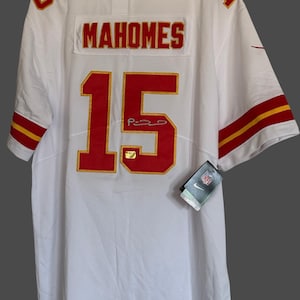 K&ouml;nnte beinhalten: Wei&szlig;es Football-Trikot mit roten und goldenen Akzenten. Das Trikot zeigt den Namen "MAHOMES" und die Nummer "15" auf dem R&uuml;cken sowie eine Unterschrift. Die &Auml;rmel haben rot-goldene Streifen. Ein Nike-Etikett ist angebracht.