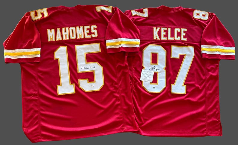 May include: Two red football jerseys. One jersey has "MAHOMES" and the number "15" in white with gold trim. The other jersey has "KELCE" and the number "87" in white with gold trim. Both jerseys have white and gold trim on the sleeves.