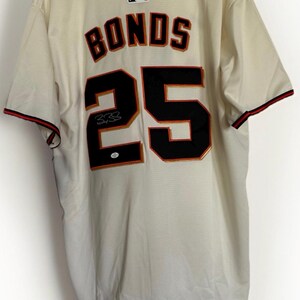 May include: Cream-colored baseball jersey with the name "BONDS" and the number "25" in black and orange. The jersey has red and black trim on the collar and sleeves, and a signature is visible.