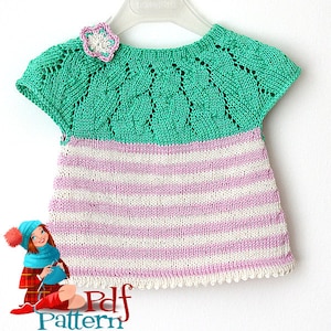 Könnte beinhalten: Ein gestricktes Babykleid mit kurzen Ärmeln. Die obere Hälfte des Kleides ist grün mit einem Spitzenmuster und einer Blumenapplikation. Die untere Hälfte des Kleides ist rosa-weiß gestreift.