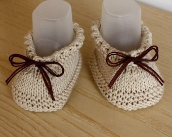 May include: A pair of beige knitted baby booties with brown ribbon ties.