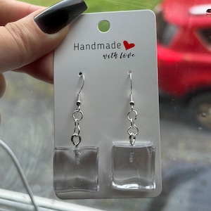 May include: Clear square earrings with silver hooks and chain links. The earrings are displayed on a white card that reads "Handmade with love" with a red heart.