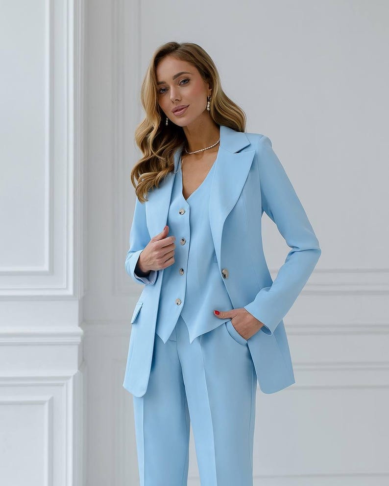May include: A light blue three-piece suit. The suit includes a blazer, vest, and trousers. The blazer has two gold buttons and two pockets. The vest has three buttons. The trousers are straight-legged. The suit is made of a smooth fabric.