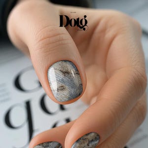 May include: Close-up of a hand with a manicure featuring a snakeskin pattern. The nail art design showcases a detailed print in shades of gray and brown, with a glossy finish. The image includes the text "Dotg Studio".