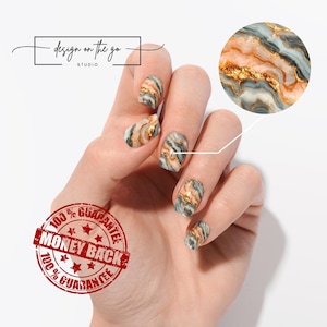 May include: Nail art with a marble design in shades of gray, peach, and gold. The nails are on a hand, with a close-up of the design in a circle. The text "design on the go STUDIO" is in the upper left corner. A red stamp says "100% GUARANTEE MONEY BACK".