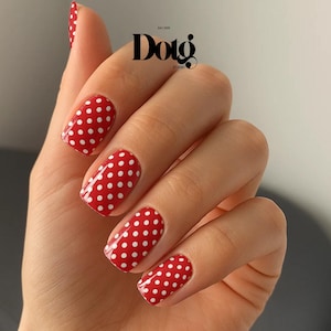 May include: Red nail polish with white polka dots. The nails are oval-shaped and glossy. The image includes the text "Dotg Studio".