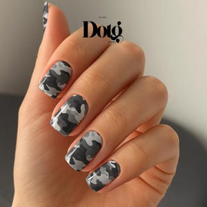 May include: A hand displaying manicured nails with a camouflage pattern in shades of gray and white. The nails are square-shaped and glossy. The image includes the text "Dotg Studio".