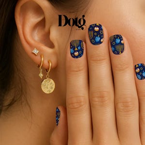 May include: Gold earrings with a star and a round pendant, and blue nail art with Hanukkah symbols. The earrings are worn on the ear. The nail art features menorahs, dreidels, and stars on a dark blue background. The image includes the text "Dotg Studio".