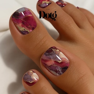 May include: Toenails featuring a glossy, marbled design in shades of deep magenta, plum, and cream, accented with thin, metallic gold veins. The design is applied to the nail surface, and the text "Doto" is visible in black near the top center.