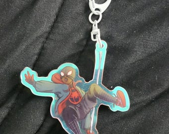 May include: A clear acrylic keychain featuring a superhero in a dynamic pose. The character is wearing a red and black suit with a blue jacket and red sneakers. The keychain has a silver clasp.