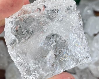 May include: A clear, rough-cut quartz crystal is held between fingers. The crystal is translucent with visible internal textures and facets. The text "CRYSTALS 4 MEDITATIONS" is visible at the bottom of the image. The crystal is a natural, raw gemstone.