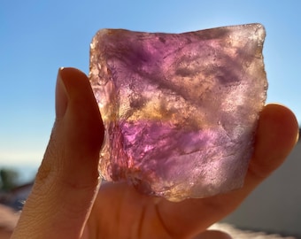 May include: A large, rough-cut amethyst crystal with a purple and yellow hue. The crystal is being held in a hand against a blue sky background. The text "CRYSTALS 4 MEDITATIONS" is visible at the bottom of the image.