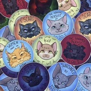 May include: A collection of round stickers featuring cat illustrations with various expressions and phrases. The stickers have a variety of colors, including blue, red, and yellow. Some stickers have text like "I scare" and "The horrors persist, yet".