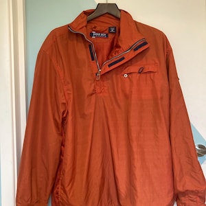 May include: An orange Bugle Boy jacket with a quarter-zip closure and a small pocket. The jacket has a stand-up collar and a drawstring at the bottom. The brand name "Bugle Boy" is visible on a tag near the collar.