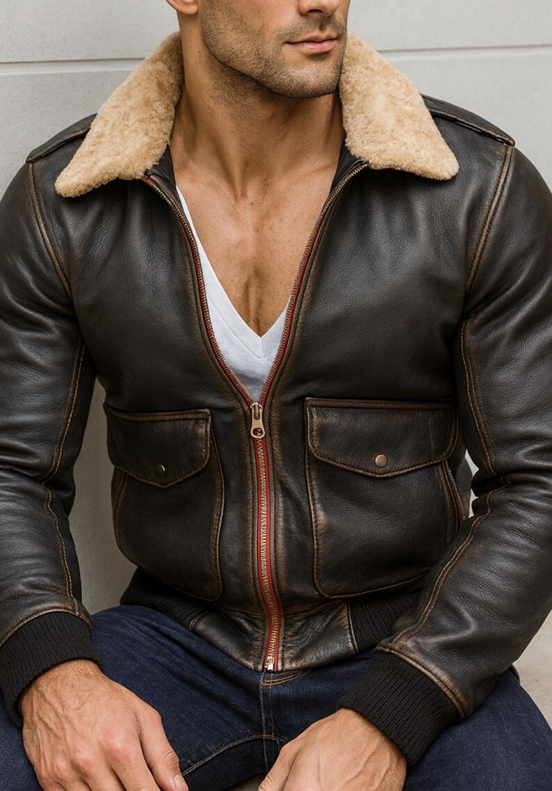 Puede incluir: Chaqueta bomber de cuero marr&oacute;n con cuello de borrego beige. La chaqueta tiene dos bolsillos delanteros, una cremallera roja y pu&ntilde;os acanalados. La chaqueta se lleva sobre una camisa blanca.