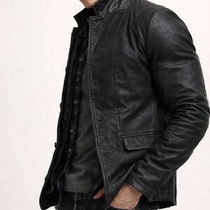 May include: Black leather jacket with a classic collar and button closure. The jacket features two front pockets and a tailored fit. The model is wearing a dark shirt and jeans. The jacket is a versatile outerwear piece.