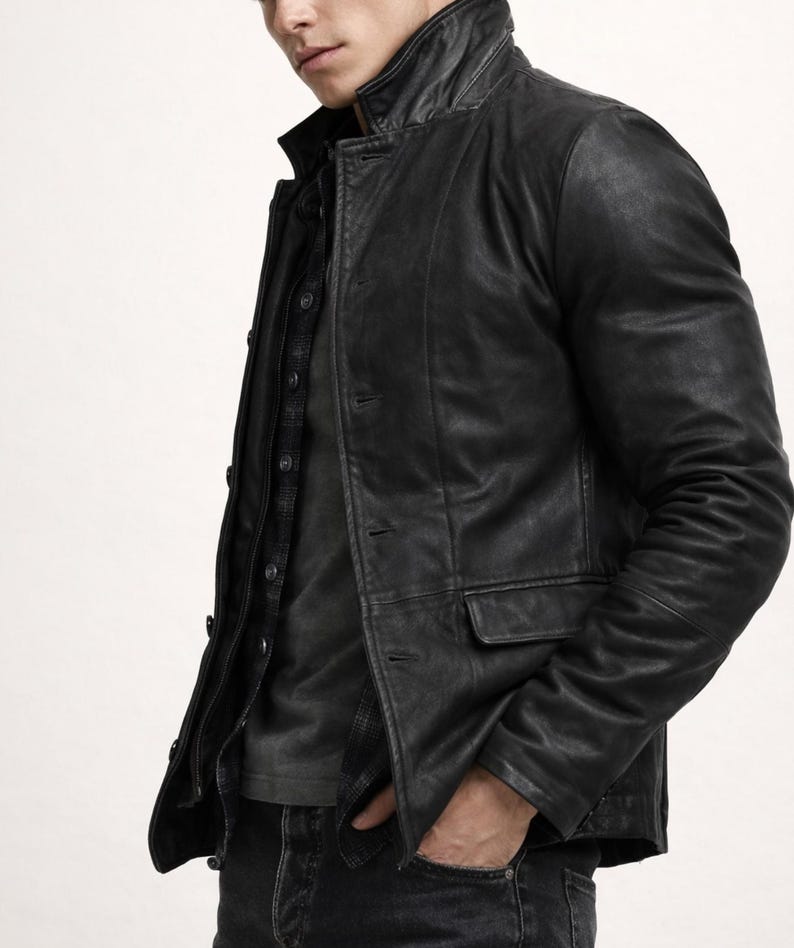 May include: Black leather jacket with a classic collar and button closure. The jacket features two front pockets and a tailored fit. The model is wearing a dark shirt and jeans. The jacket is a versatile outerwear piece.