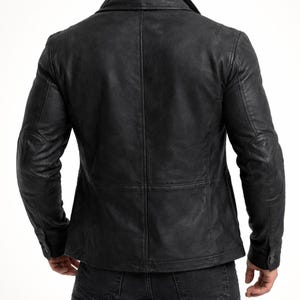 May include: A black leather jacket with a textured finish. The jacket features a notched collar, buttoned cuffs, and a tailored fit. The back view showcases the jacket's seams and design details, offering a classic and stylish look.