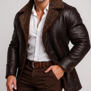 May include: A brown leather coat with a shearling collar and lining. The coat has a button closure and a brown leather belt. The model is wearing a white shirt and brown pants. The coat is a classic style.