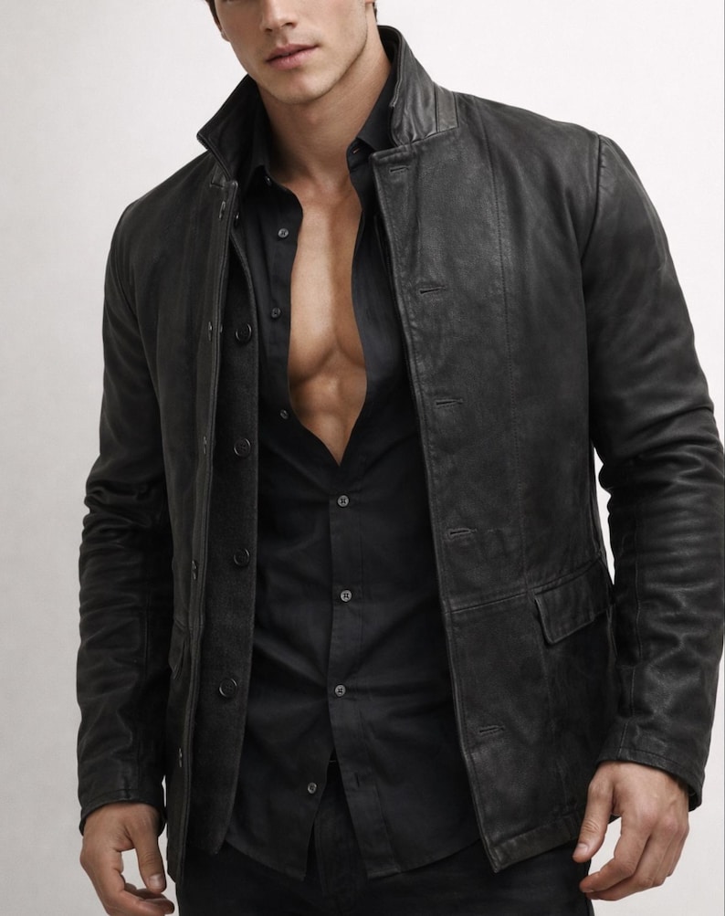 May include: Black leather jacket with a button-up front and two front pockets. The jacket is worn over a black button-down shirt. The collar of the jacket is a stand-up style.