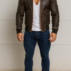 Puede incluir: Chaqueta bomber de cuero marr&oacute;n con cuello de borrego beige, dos bolsillos delanteros y pu&ntilde;os y dobladillo de canal&eacute; negros. La chaqueta se lleva sobre una camiseta blanca con cuello en V y se combina con vaqueros azul oscuro y botas marrones.