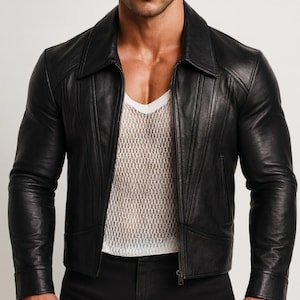 May include: A black leather jacket with a notched collar and a zip-up front. The jacket has vertical stitching details on the front and sleeves. The model is wearing a white mesh shirt underneath. The jacket is a classic outerwear piece.